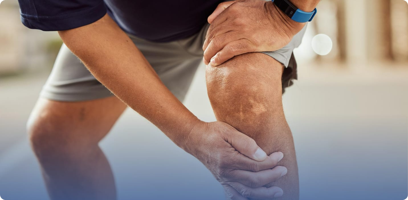 Older man in running shorts bending forward and holding his painful knee