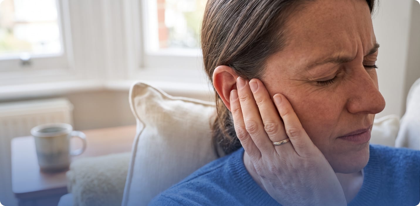 Woman on a sofa pressing a hand to her ear and wincing from ringing in the ear